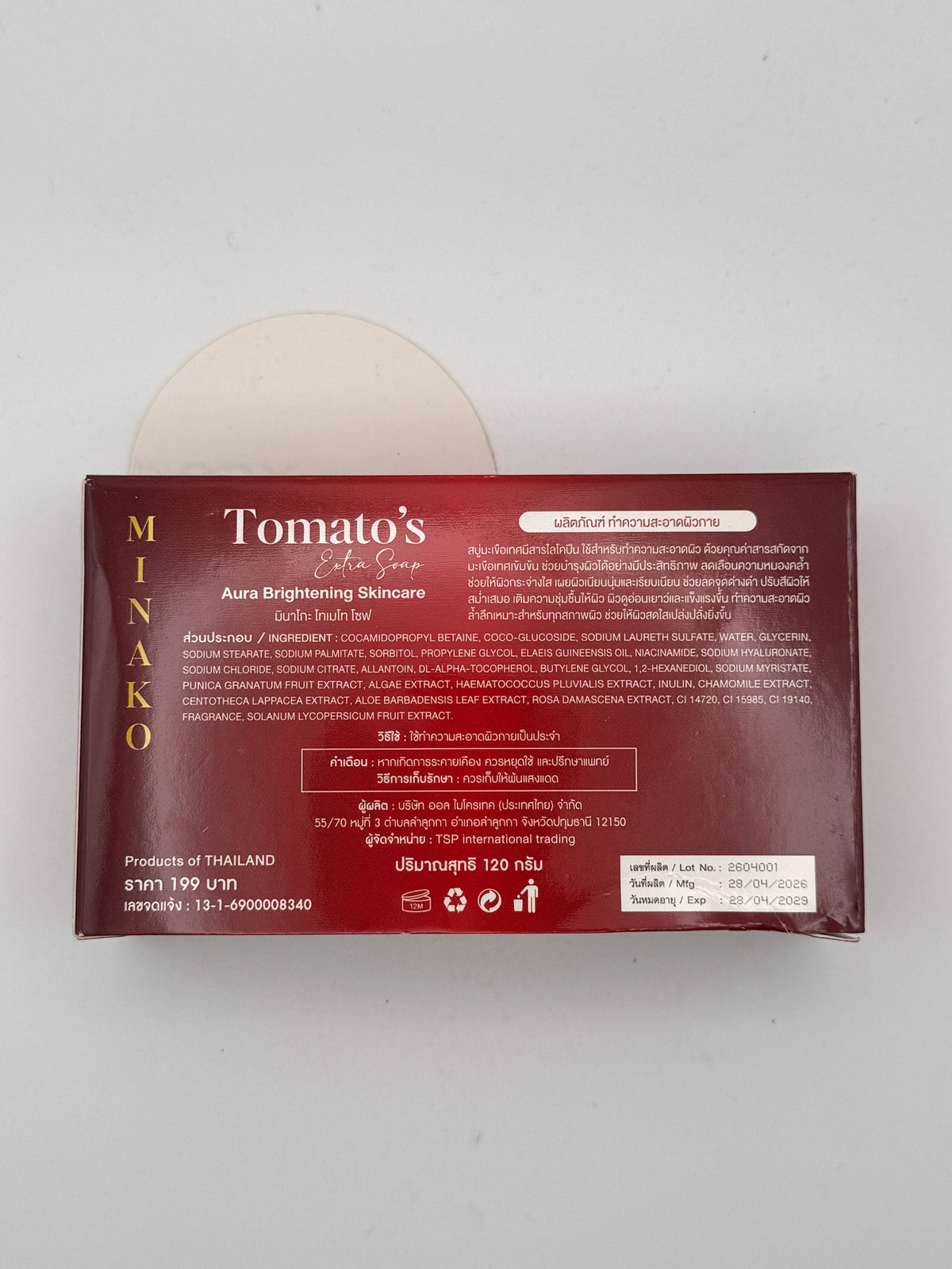 Back of the Minako Tomato's Extra Soap box next to the round cream-coloured bar, showing the Thai ingredient list with tomato fruit extract, niacinamide and sodium hyaluronate, plus directions and warnings